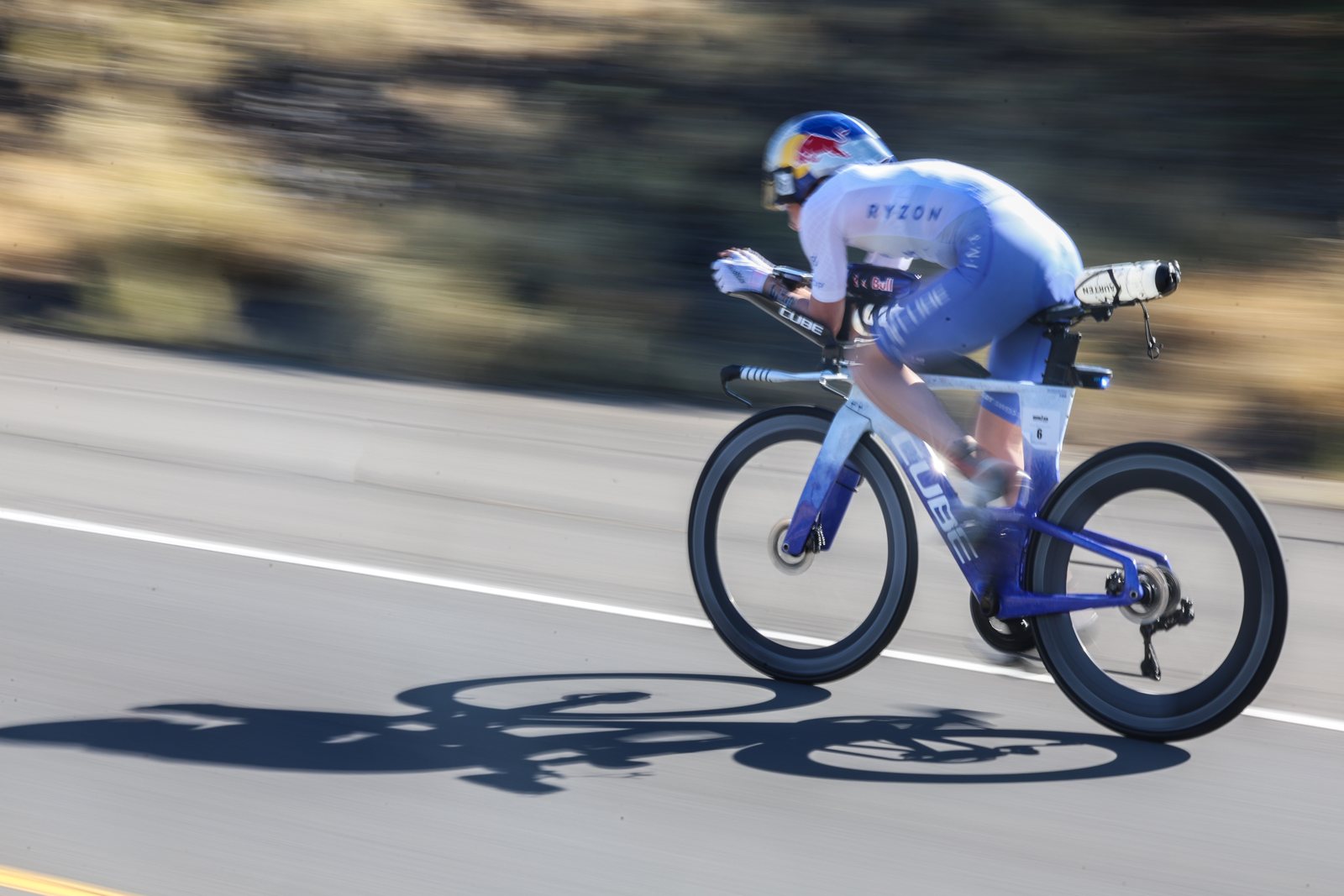 2026 Kona 女子職業選手以計時姿勢騎在熔岩公路上，路面映著人車的影子